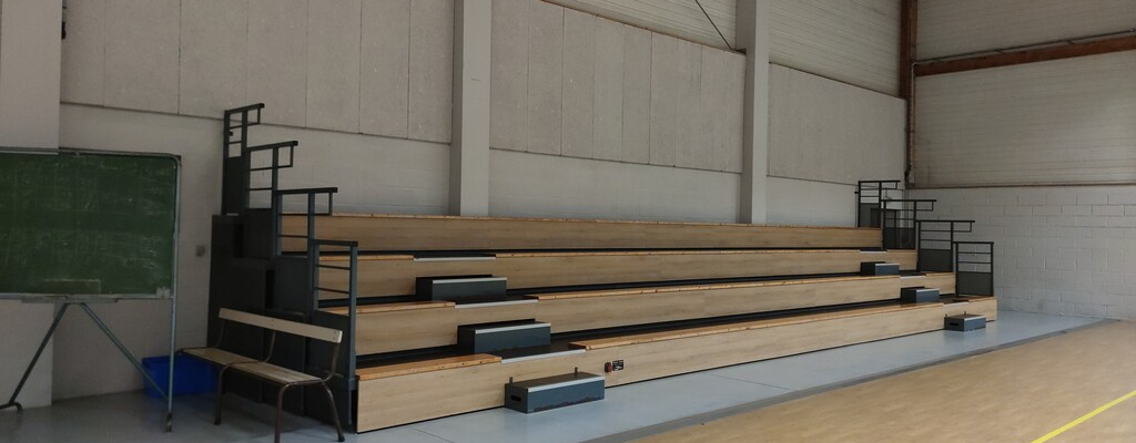 Gymnase avec gradins, tableau et parquet.