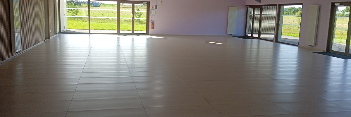 Salle vide avec sol en carrelage, grandes fenêtres et plafonniers.