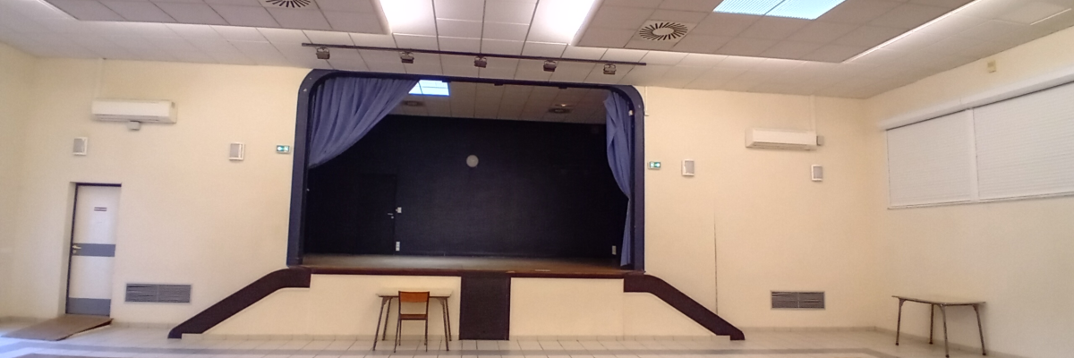 Salle avec scène, écran, projecteur, tabourets, climatiseurs et lumières.