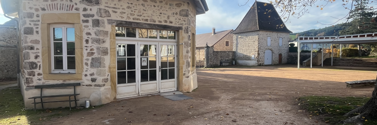 Bâtiment en pierre avec porte, fenêtre, banc et cour.