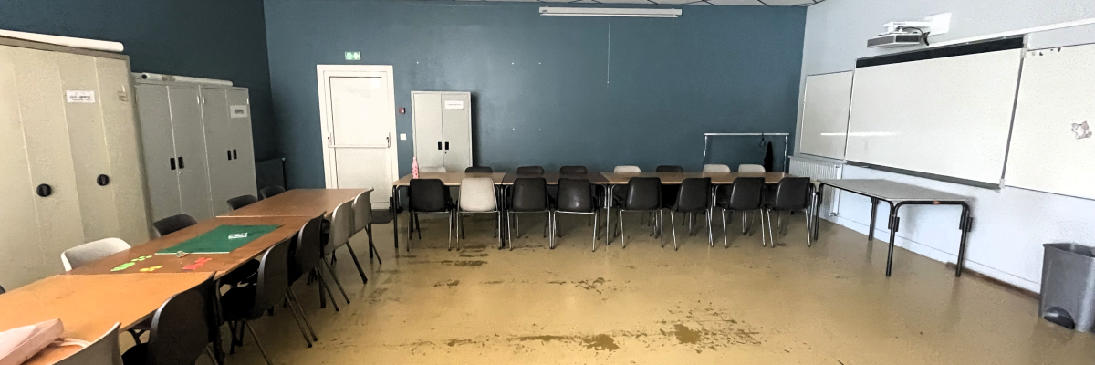 Salle avec tables, chaises, armoires, tableau blanc et projecteur.