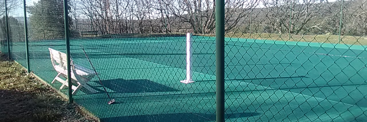 Terrain de tennis avec filet, chaises et clôture.