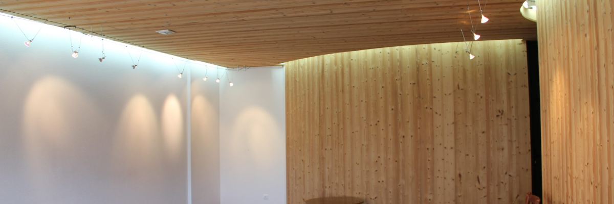 Pièce avec murs en bois, sol noir, table ronde, chaises, éclairage suspendu.