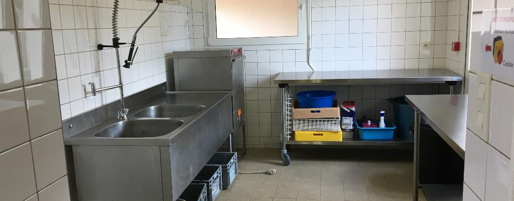 Cuisine avec évier, robinet, plan de travail, étagères, produits de nettoyage et fenêtre.