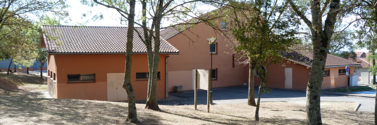 Bâtiment orange avec toits en tuiles, arbres, parking.