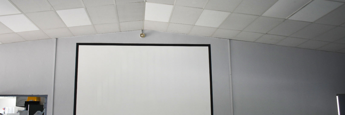 Salle avec écran, vidéo projecteur suspendu, table, chaises et matériel divers.