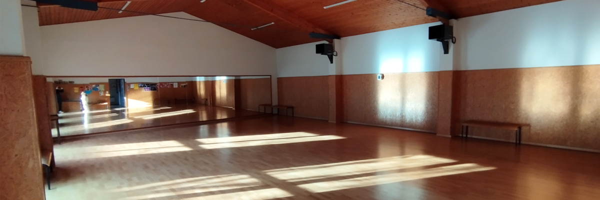 Salle avec plancher en bois, bancs, miroirs et plafonnier.