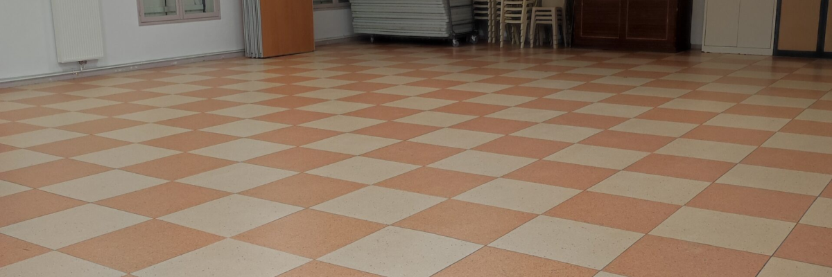 Salle vide avec sol carrelé, chaises empilées, porte en bois et porte blanche.