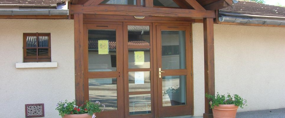 Entrée avec double porte en bois, fenêtres, pots de fleurs et auvent en bois.