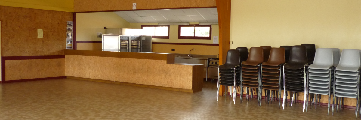 Salle polyvalente avec chaises, plan de travail, évier et fours encastrés.