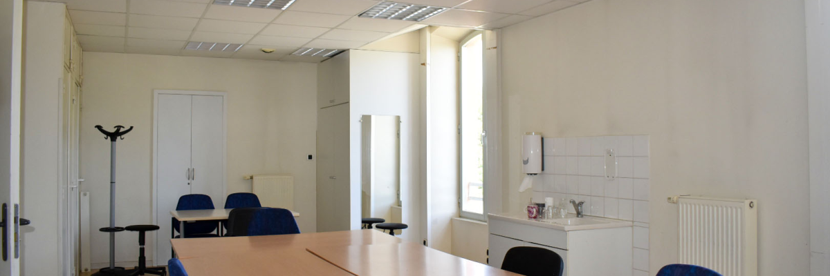 Salle de réunion avec table, chaises, porte-manteau, lavabo et radiateur.