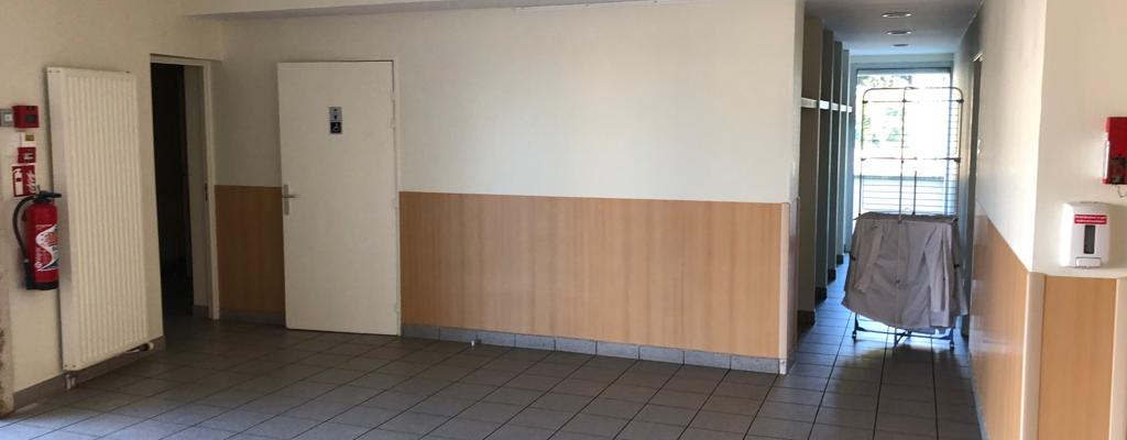 Salle vide avec radiateur, extincteur, porte, chariot couvert.