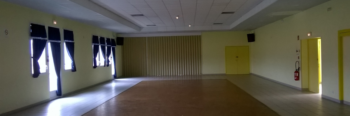 Salle vide avec fenêtres, porte, extincteur, et projecteur plafond.