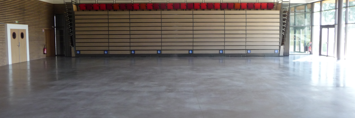 Salle vide avec murs en bois, sol lisse, portes vitrées et plafond éclairé.