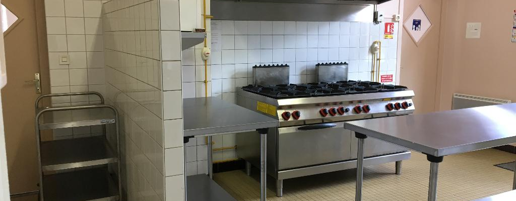 Cuisine avec plaques de cuisson, hotte, chariot, plans de travail et carrelage mural.