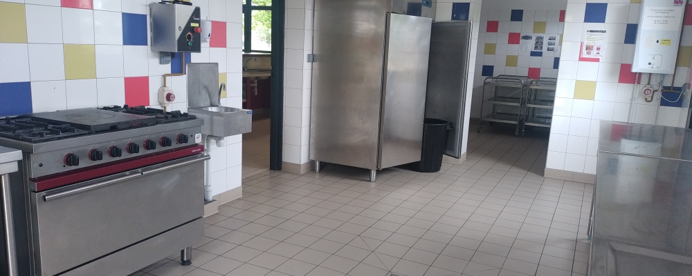 Cuisine professionnelle avec four, plinthe électrique, frigo, étagères, et murs carrelés.