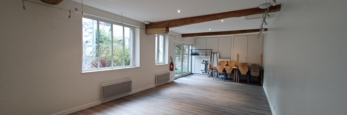 Salle avec poutres apparentes, fenêtres, radiateurs, et matériel de gymnastique au fond.