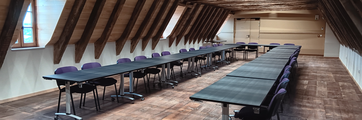 Salle avec tables, chaises et poutres apparentes.