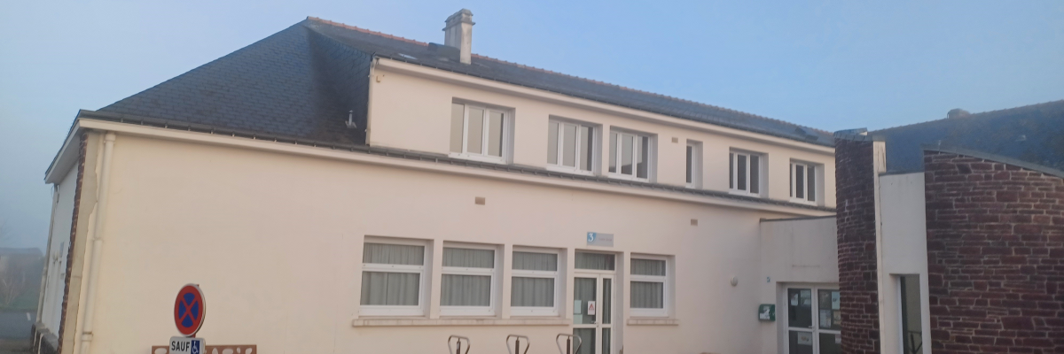 Bâtiment avec fenêtres, portes et stationnement. Panneau d'interdiction et banc visible.