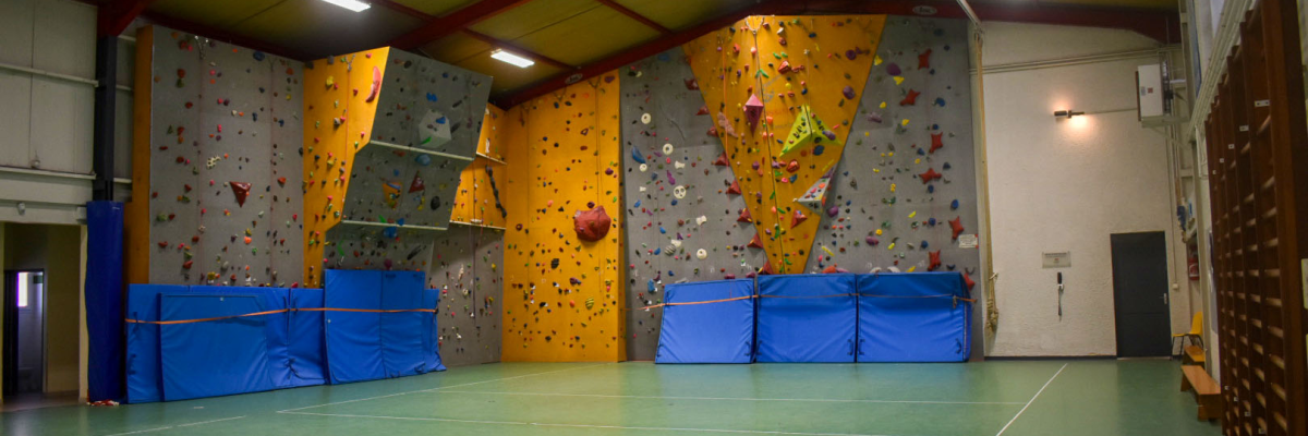 Salle d'escalade avec murs d'escalade, tapis de sécurité, sol vert et éclairage.