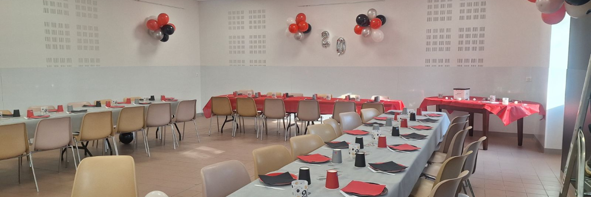 Salle de fête avec tables, chaises, serviettes, verres, ballons et décorations murales.