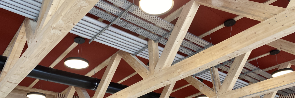 Poutres en bois, plafond rouge, lumières, conduits noirs.