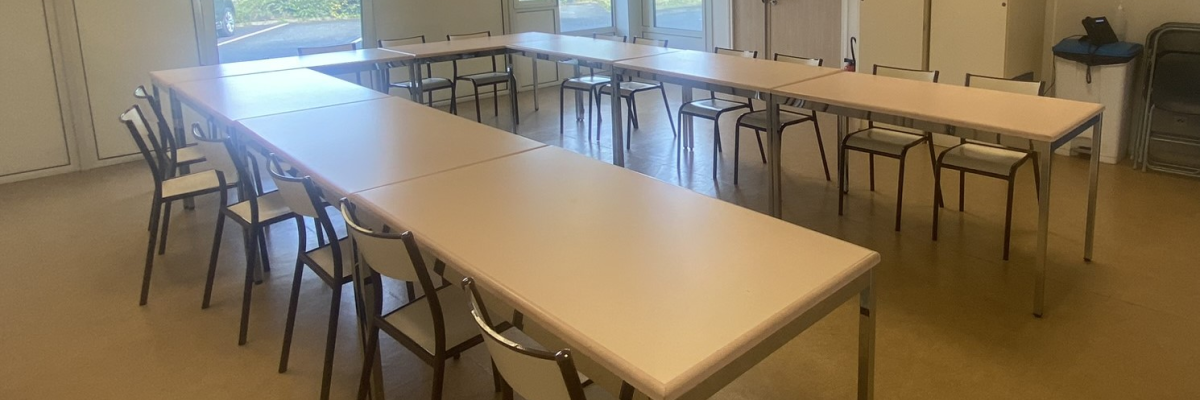 Salle de réunion avec tables, chaises, porte et détecteur de fumée.