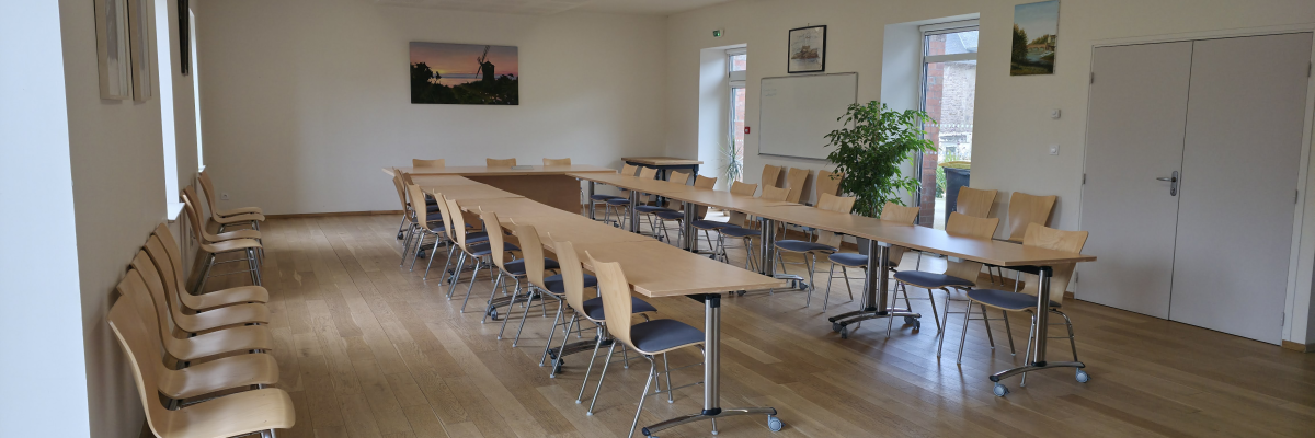 Salle de réunion avec tables, chaises, tableau blanc, plantes, portes et éclairage.