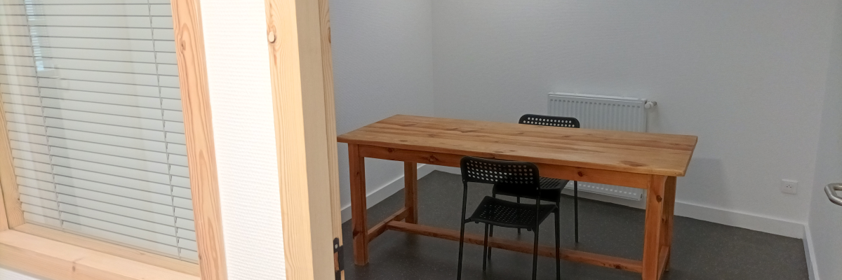 Pièce avec table en bois, deux chaises noires, radiateur et stores.