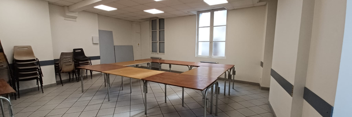 Salle avec tables, chaises, fenêtres et éclairage au plafond.