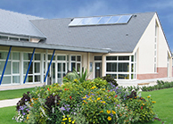 Bâtiment avec panneaux solaires, porte en verre et buissons devant.