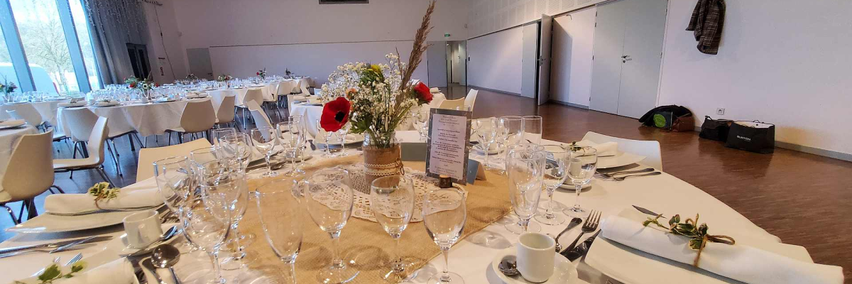 Salle avec tables, chaises, vaisselle, verres et fleurs.