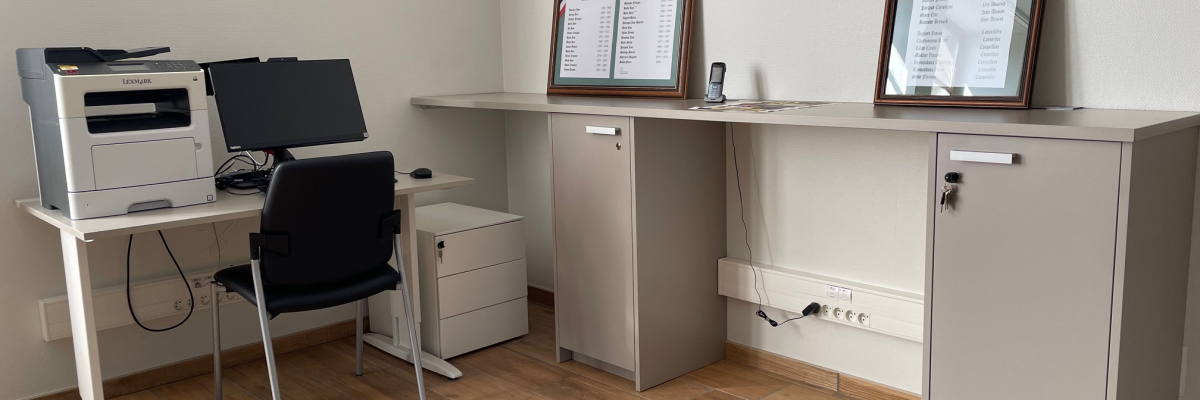 Bureau avec ordinateur, imprimante, chaise, classeurs, étagère et cadres.