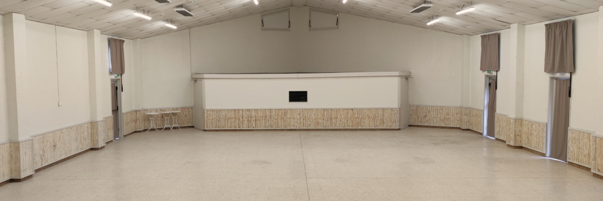 Salle vide avec éclairage suspendu, murs de briques et plancher en bois.