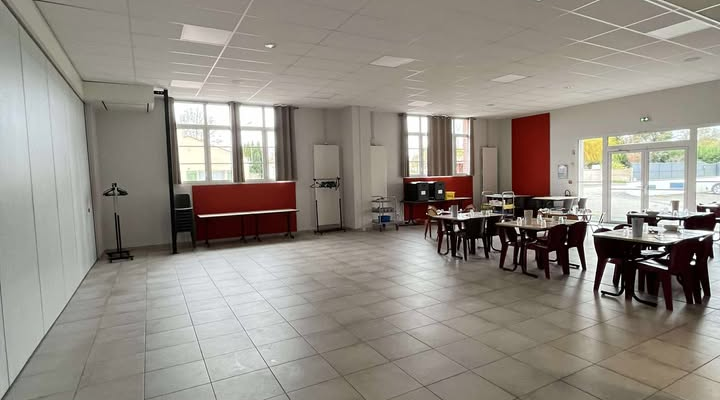 Salle avec tables, chaises, placard et fenêtres.