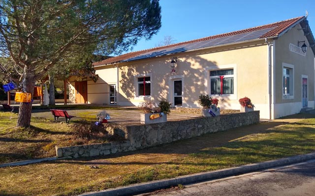 Bâtiment avec jardin, arbres, bancs et fleurs en pot.