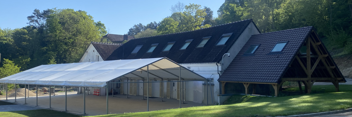 Bâtiment avec structure en bois, toit incliné, abri extérieur et parking adjacent.
