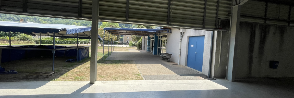 Atelier avec porte bleue, banc, sol en béton et toit métallique.