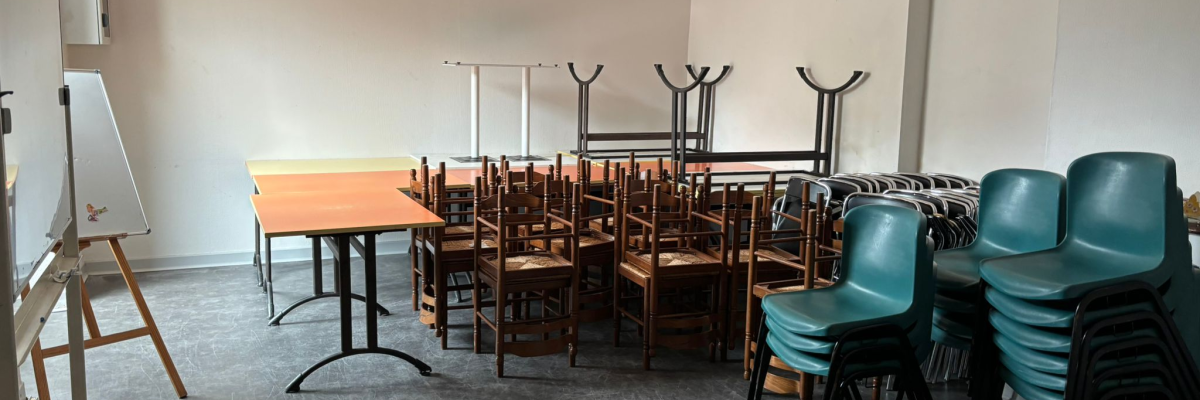 Salle avec tables, chaises, chevalet et tableau blanc.
