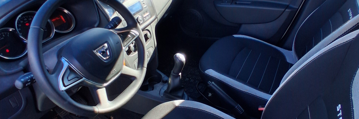 Intérieur de voiture avec volant, sièges, tableau de bord, rétroviseur.