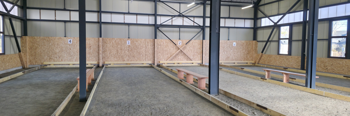 Hangar avec sol en béton, murs en bois, piliers métalliques et toit métallique.