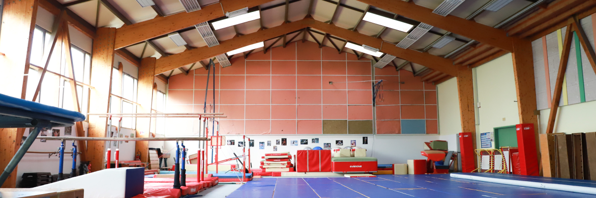 Salle de gymnastique avec agrès, tapis, table et tableau.