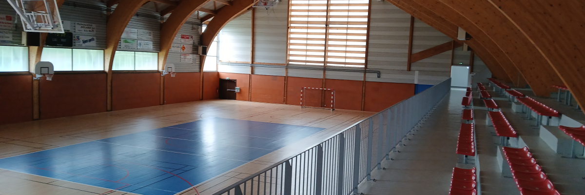 Salle de sport avec terrain, paniers, gradins et filet de volley.