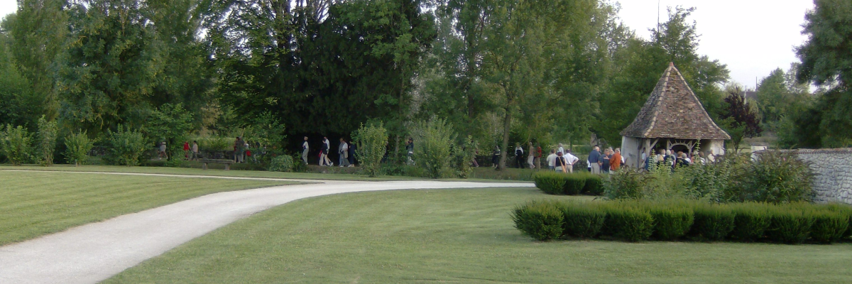 "Jardin avec sentier, pelouse, arbres, buissons, et petite cahute. Groupe de personnes à l'arrière-plan."