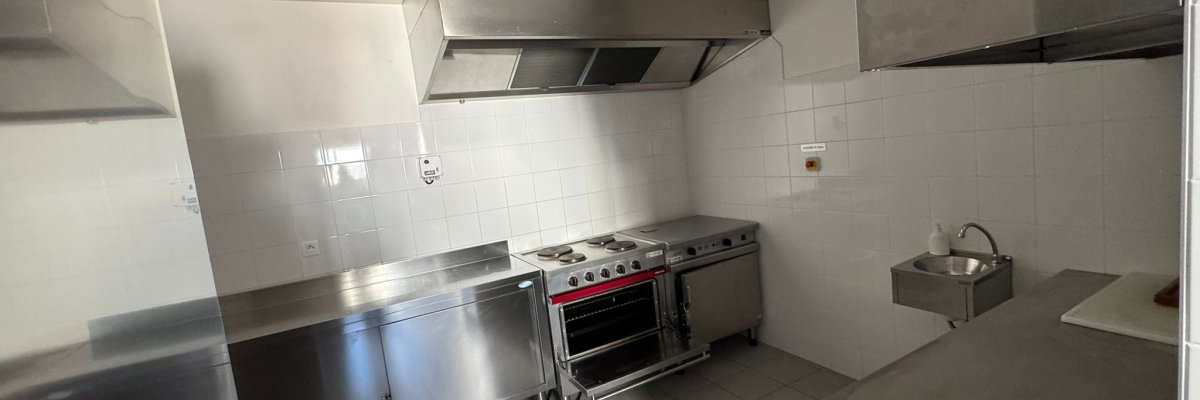 Cuisine avec plans de travail en acier inoxydable, fourneaux, hotte, évier et carrelage mural.