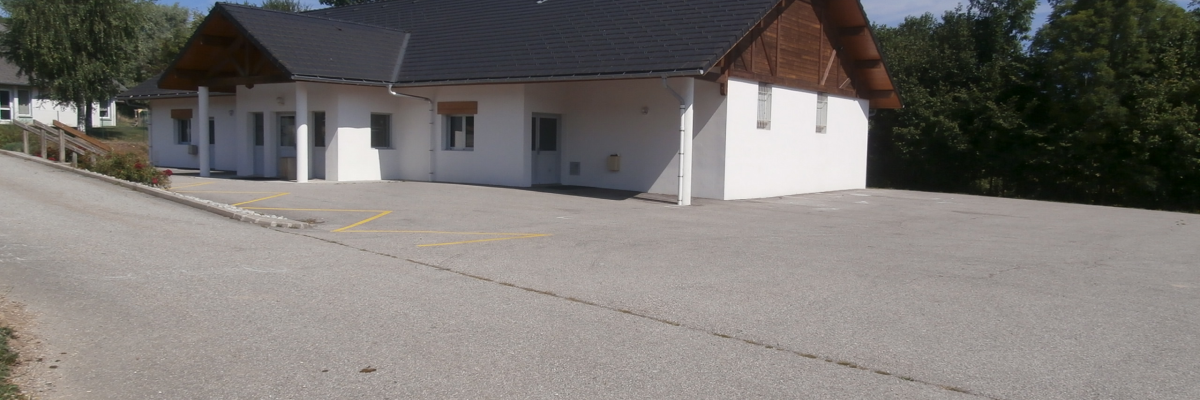 Un bâtiment blanc avec un toit en pente, une allée de gravier et des voitures garées.