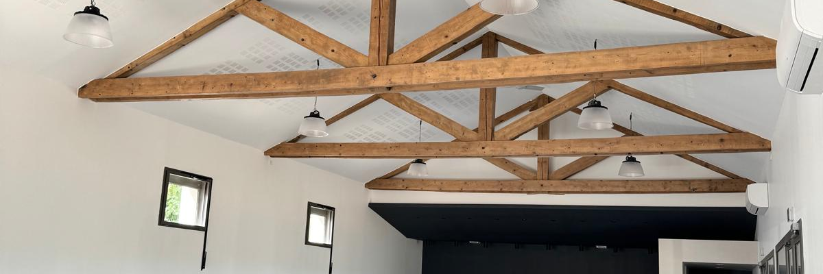 Salle avec poutre en bois, sol carrelé, table, comptoir et éclairage suspendu.