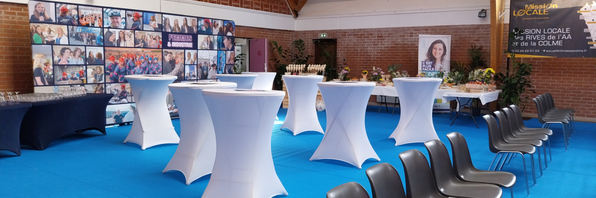 Salle avec tables hautes, chaises, écrans, murs en brique, sol bleu.