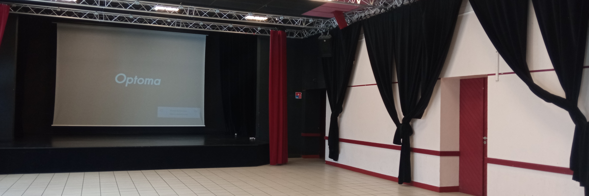 Salle avec écran, projecteur, structures métalliques, rideaux et sol carrelé.