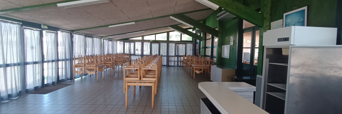 Cafétéria avec tables, chaises, frigo, comptoir, et fenêtres.